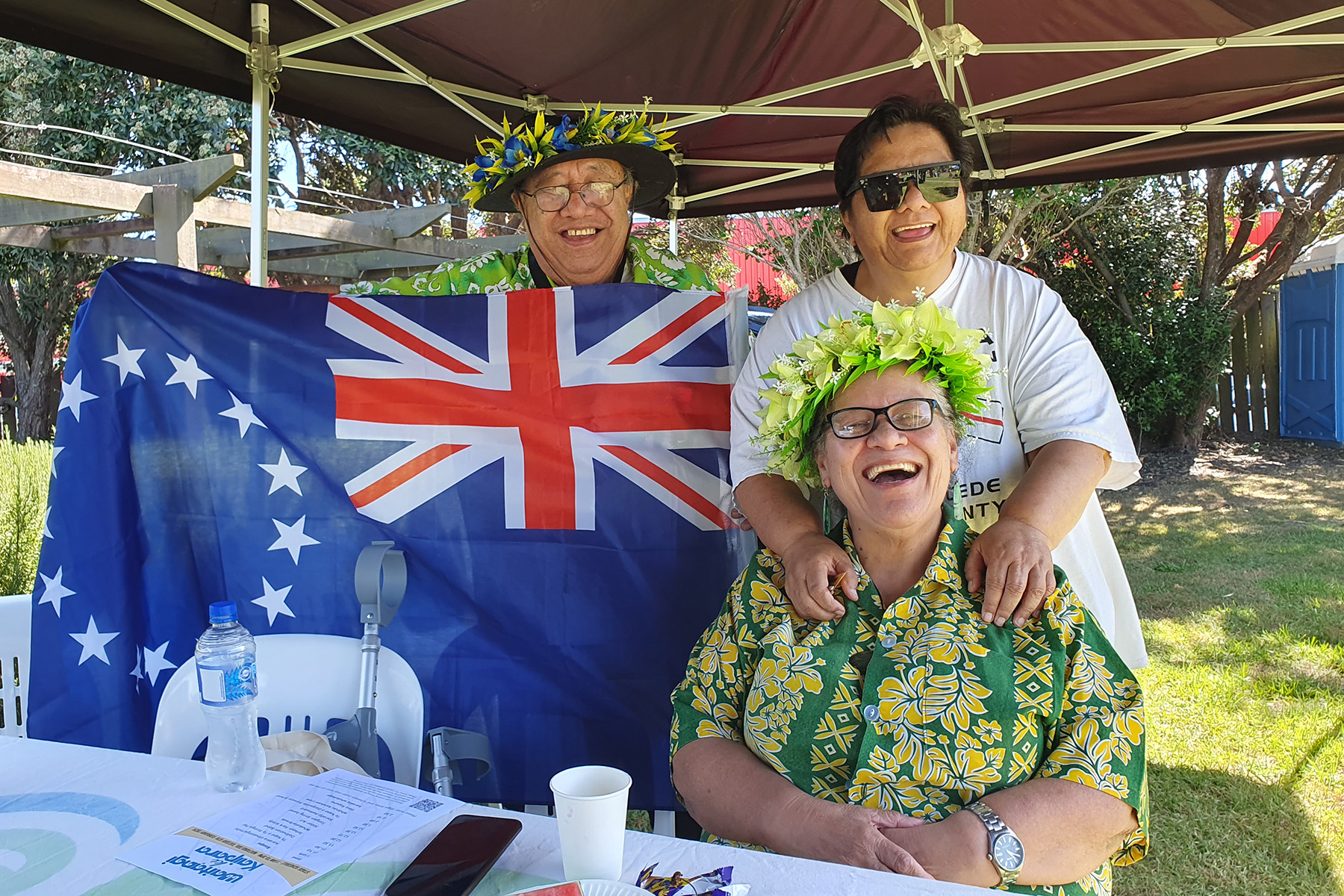 Three people behind a table with one holding up a flag while under a tent.