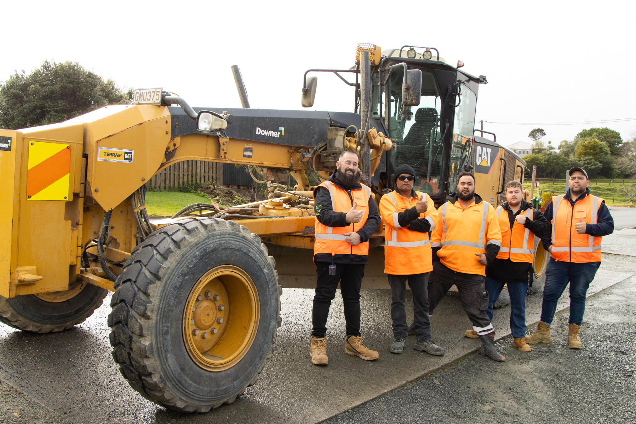 Some of the Downer roading team stand in front of a road grader