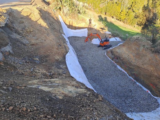 Image showing orange digger working with gravel in a large excavated area below the road.